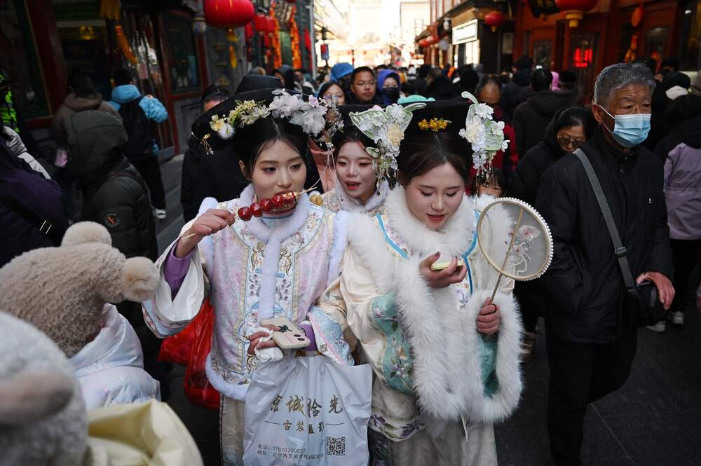Three woman eat snack food as the walk through a popular shopping street wearing traditional clothing on the sixth day of the Lunar New Year in Beijing on February 3, 2025. Bloomberg Three woman eat snack food as the walk through a popular shopping street wearing traditional clothing on the sixth day of the Lunar New Year in Beijing on February 3, 2025. Bloomberg