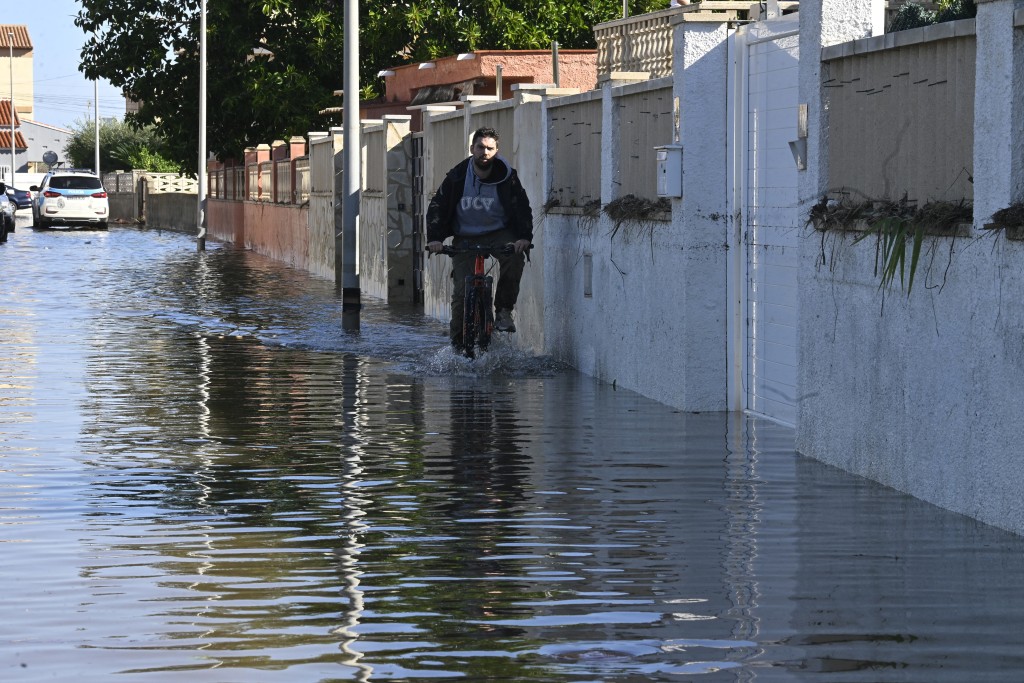 Photo by JOSE JORDAN / AFP  A cyclist drives in a flooded street following torrential downpours in Oliva, in the Valencia region, eastern Spain on October 20, 2026.
