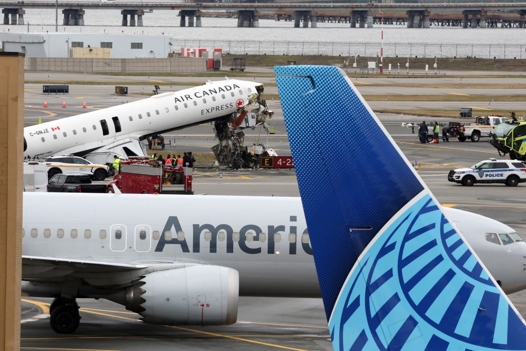 Photo by TIMOTHY A. CLARY / AFP  An American Airlines jet taxis past the Air Canada Express CRJ-900 that collided with a Port Authority fire truck at LaGuardia Airport in New York, after the airport resumed operations on March 23, 2026.