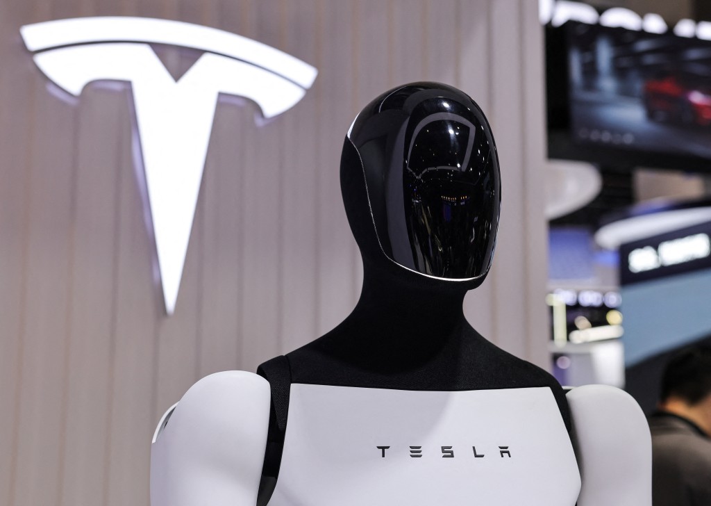 A Tesla Optimus robot is displayed next to a logo at the company? booth at the 8th China International Import Expo (CIIE) in Shanghai, China, November 6, 2025.REUTERS/Maxim Shemetov