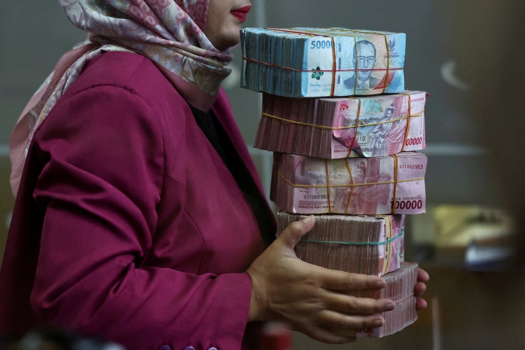 A teller holds rupiah bank notes at a money changer in Jakarta, Indonesia, April 9, 2025. Picture taken through glass. REUTERS