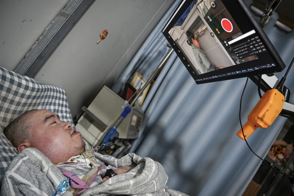 Photo by JADE GAO / AFP  This photo taken on December 16, 2025 shows Li Xia, who has Duchenne muscular dystrophy, guiding his mother through the circuit operation via a video monitoring app from his bed in southwestern China's Chongqing municipality.