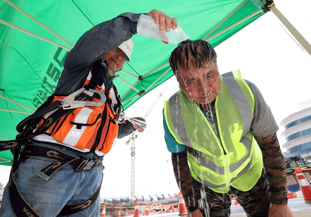 A worker pours cold water in a plastic bottle on his colleague in order to cool off him at a construction site in Incheon, South Korea August 2, 2023. Yonhap/via REUTERS