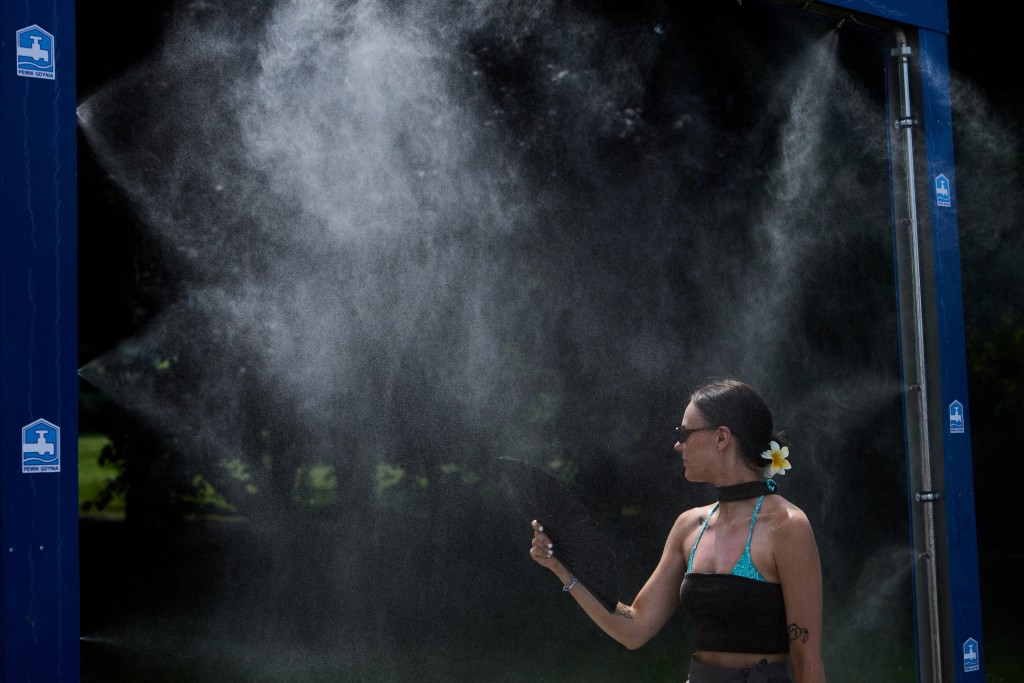 A woman uses a hand fan as she cools off at a mist dispenser during a heatwave, in Gdynia, Poland (Reuters)