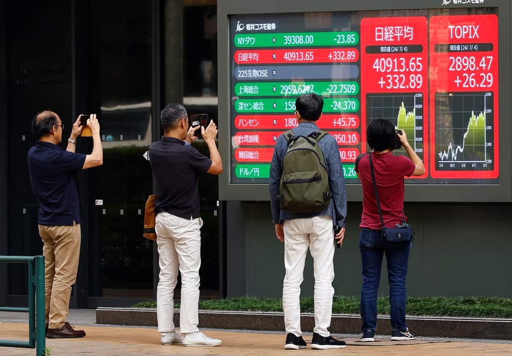 People take pictures of a monitor displaying Topix share average and Nikkei share average outside a brokerage in Tokyo, Japan, July 4, 2024. REUTERS