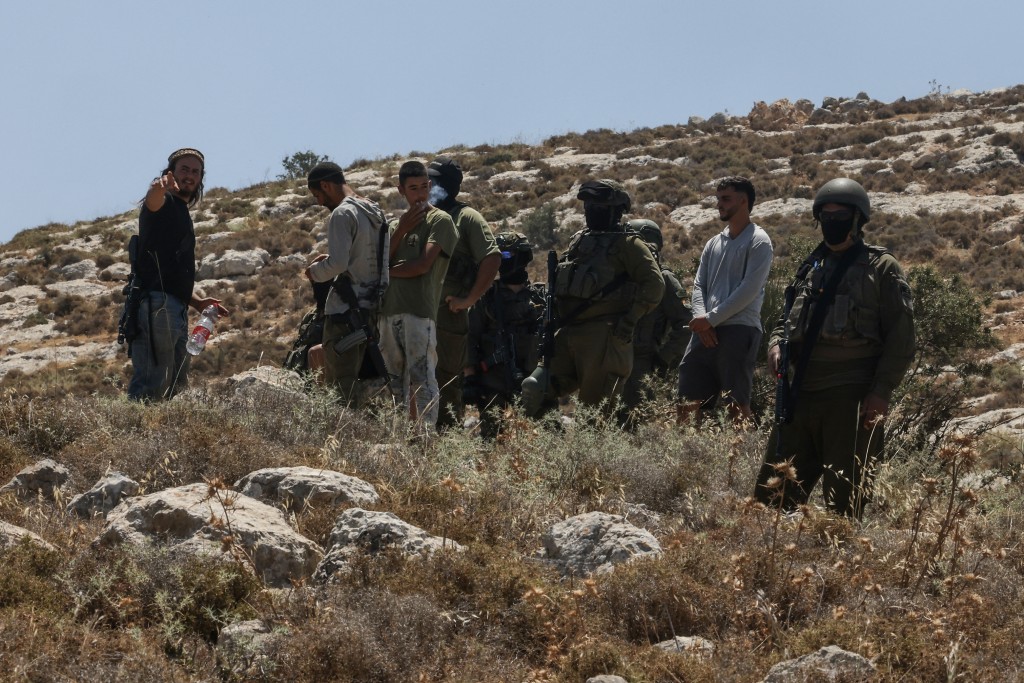 Israeli forces and armed settlers guard a bulldozer reportedly operating on Palestinian lands as local Palestinian landowners (unseen) gather in protest against land confiscations near the village of Dura, west of Hebron in the Israeli-occupied West Bank, on June 9, 2026. (Photo by HAZEM BADER / AFP)