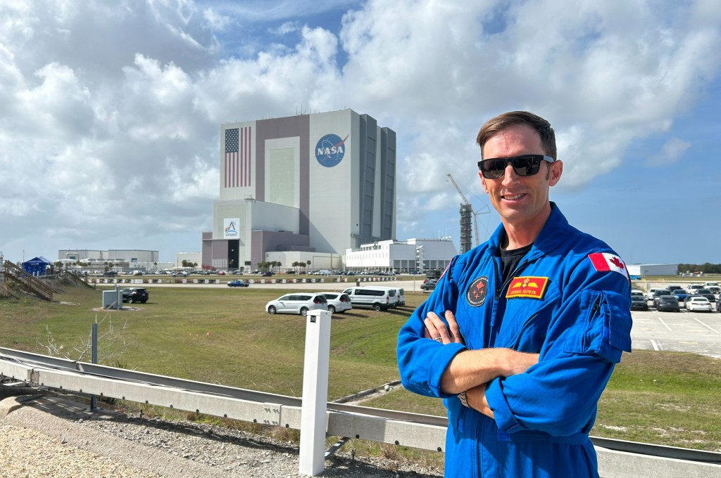 Photo by CHARLOTTE CAUSIT / AFP  The Vehicle Assembly Building is seen in the distance as Canadian astronaut Joshua Kutryk poses for a portrait at NASA's Kennedy Space Center, Florida on March 30, 2026.