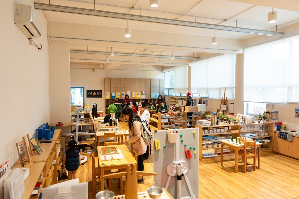 Families explore the thoughtfully designed learning space in an inviting AIP classroom, engaging with Montessori materials.