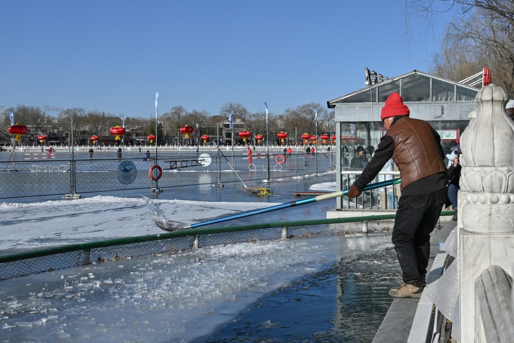 Photo by ADEK BERRY / AFP  A man cleans ice as winter swimming enthusiasts swim at the Houhai Lake of the Shichahai scenic area in Beijing on January 20, 2026.