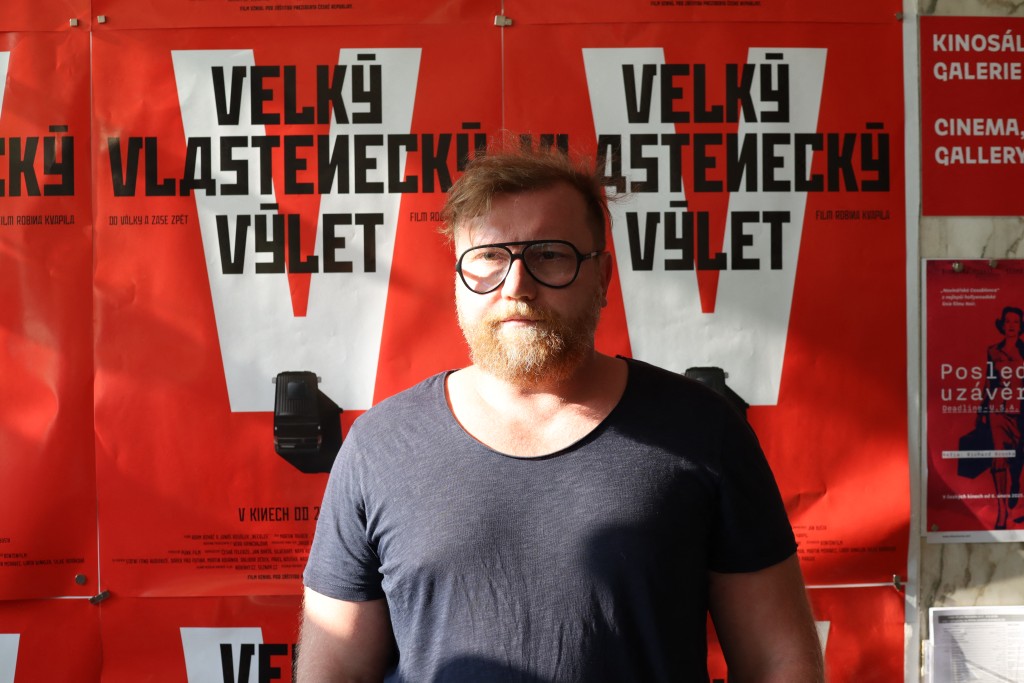 "Great Patriotic Trip" movie director Czech Robin Kvapil poses in front of the film poster ahead of a screening for journalists in Prague, Czech Republic, on August 6, 2025. Two men and a woman driven by disinformation and denying the Russian invasion of Ukraine are the unlikely protagonists of a Czech documentary due to premiere this month. (Photo by Jan FLEMR / AFP)
