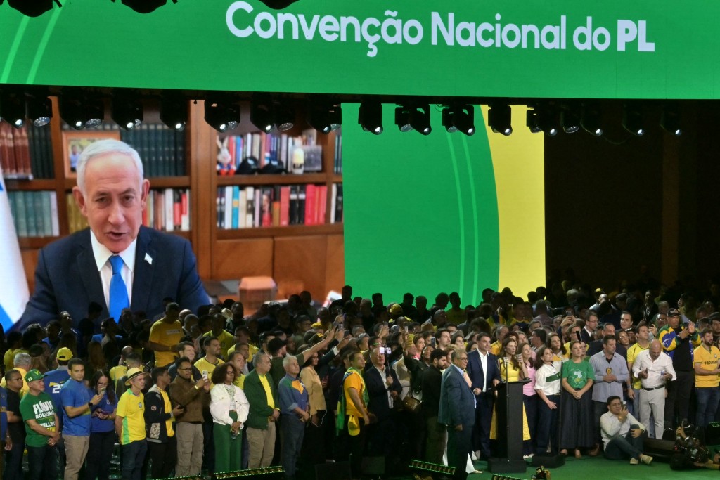 Photo by NELSON ALMEIDA / AFP. Israel's Prime Minister Benjamin Netanyahu speaks via videoconference to support the candidacy of right-wing presidential hopeful Flavio Bolsonaro during the Liberal Party (PL) convention, in Sao Paulo, Brazil on July 25, 2026.