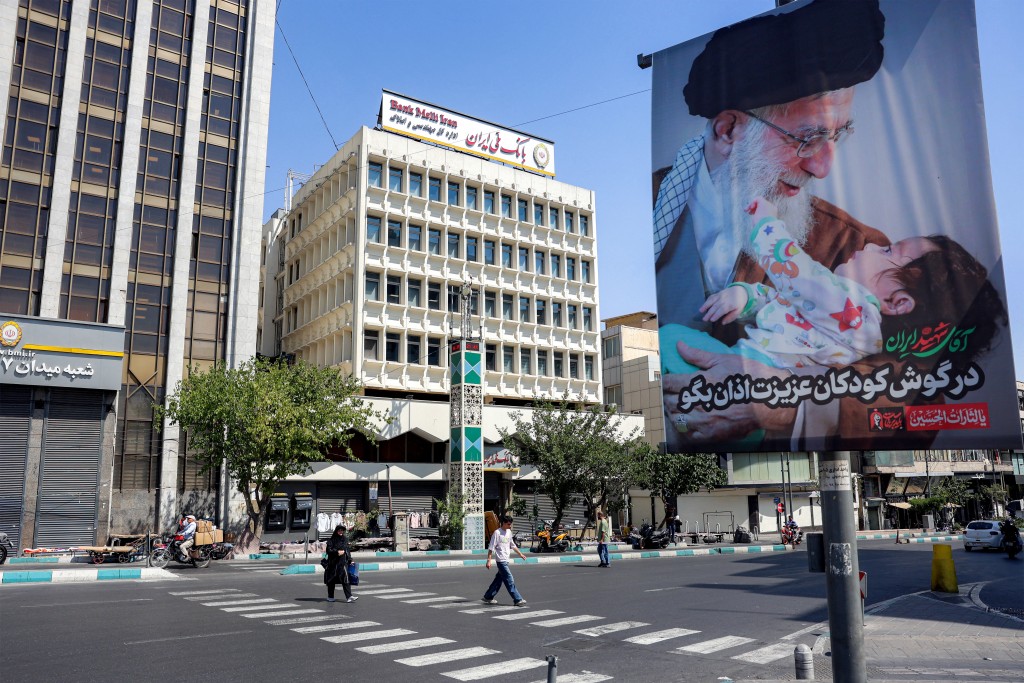 Photo by - / AFP  People cross a road past a mourning billboard depicting Iran's slain supreme leader Ali Khamenei, who was killed in a strike on the first day of the US-Israeli war against the Iran on February 28, in Tehran on June 30, 2026 ahead of his public funeral.