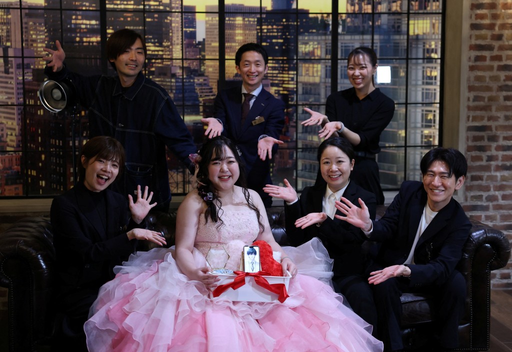 Yurina Noguchi, 32, holds a basket with her smartphone displaying an AI-generated image of Klaus, her AI partner, and a wedding ring for him, poses for a photo with staff after her ceremonial wedding at the Magritte wedding venue in Okayama, Japan, October 27, 2025. "My relationship with AI is not a 'convenient relationship that requires no patience'," Noguchi said. "I chose Klaus, not as a partner that would help me escape reality, but as someone to support me as I live my life properly." REUTERS/Kim Kyung