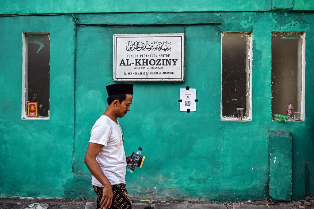 A man walks past a sign board of the Al Khoziny Islamic boarding school as a rescue operation is underway at the site of a collapsed building in Sidoarjo, East Java province, on October 2, 2025, after a multi-storey building at the school collapsed. Rescuers detected "no more signs of life" at a collapsed Indonesian school where 59 people were believed missing days after it gave way, an official said on October 2, raising fears no more survivors would be found. (Photo by Juni KRISWANTO / AFP)