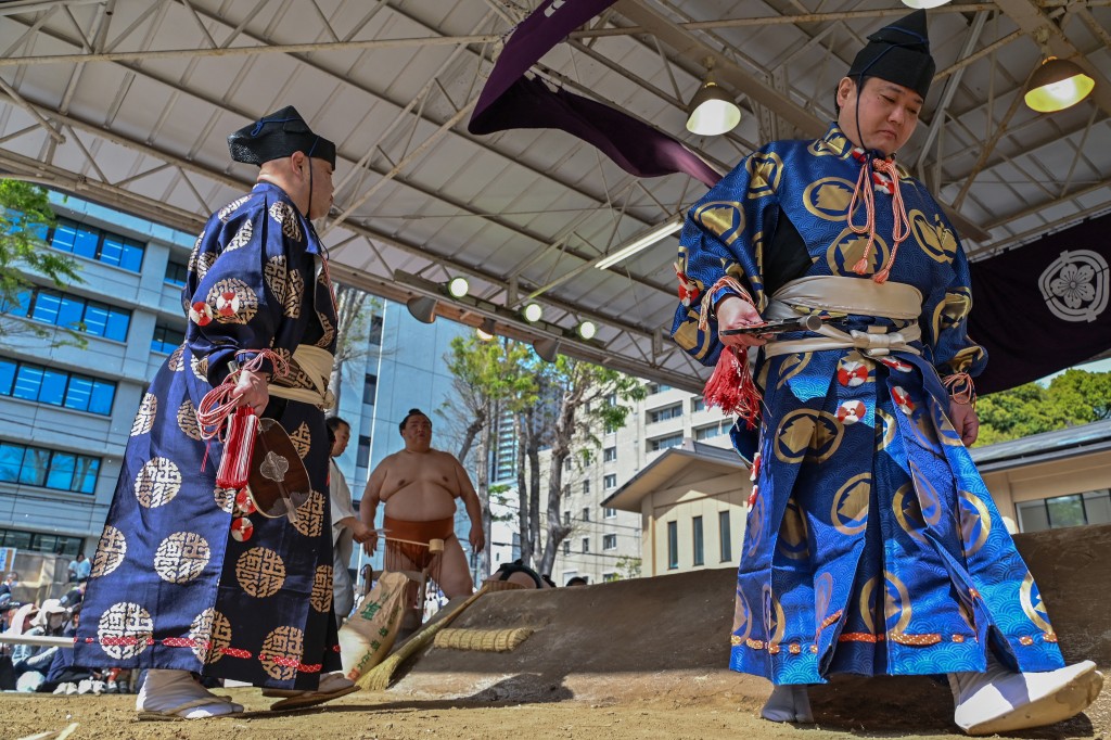 Photo by RICHARD A. BROOKS / AFP  A sumo "gyoji" (R), or referee, leaves the ring as another (L) takes his place during the annual "honozumo", a ceremonial one-day sumo exhibition for spectators held at Yasukuni Shrine in Tokyo on April 15, 2024.