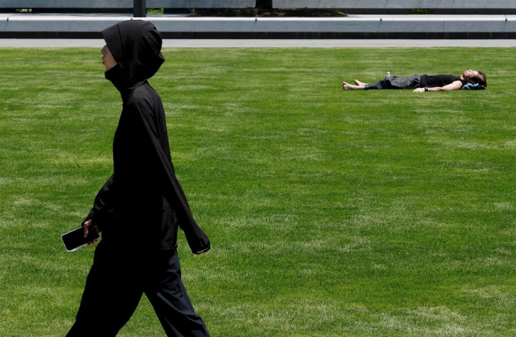 A woman wearing a sun-protective outfit walks past a man sunbathing on the grass at a park during a heat wave in Tokyo, Japan, July 15, 2026. REUTERS/Kim Kyung-Hoon