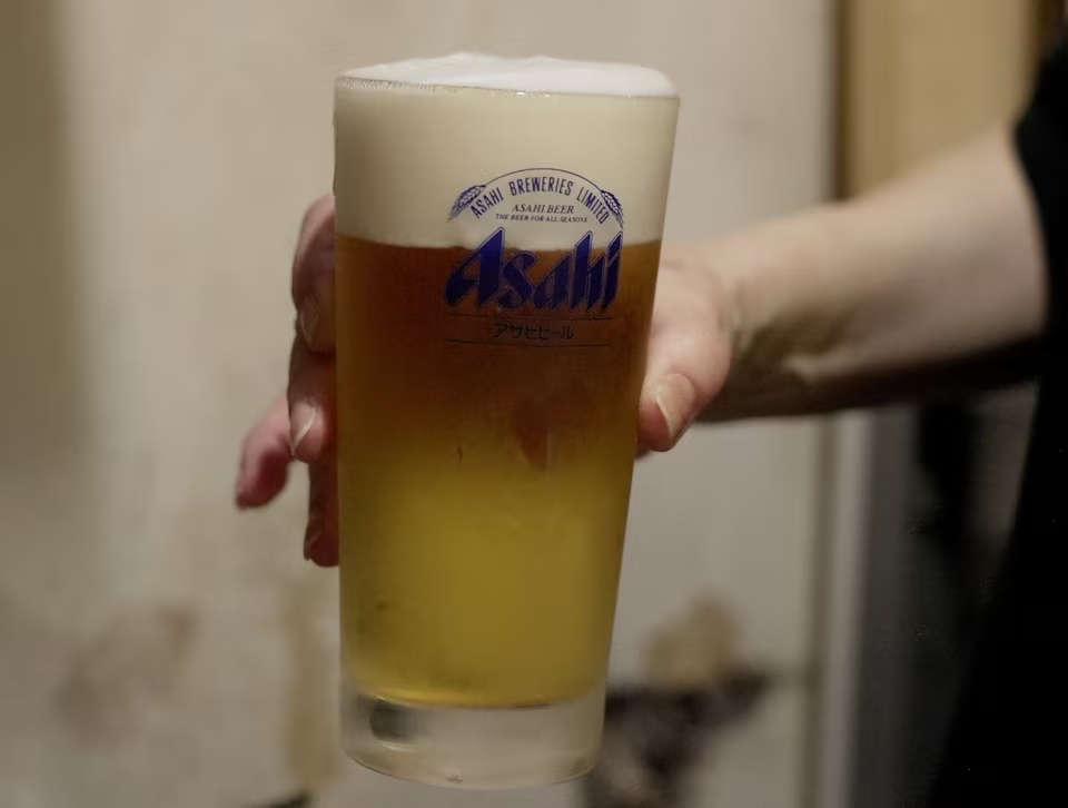 A staff of a restaurant Kushiyaki Tosaka holds a freshly poured glass of Asahi Super Dry beer at the restaurant in Tokyo, Japan, October 3, 2025. REUTERS/Joseph Campbell 