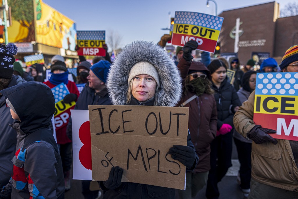 A protester holds an sign as she marches through frigid conditions, with temperatures near 10 degrees Fahrenheit (minus 12 Celsius), in a neighborhood in Minneapolis, Minnesota, on December 20, 2025, where many Somali, Latino and Hispanic immigrants live and work, during the "MN Love Our Immigrant Neighbors - ICE Out of MN!" rally calling for the removal of US Immigration and Customs Enforcement from Minnesota. (Photo by Kerem YUCEL / AFP)