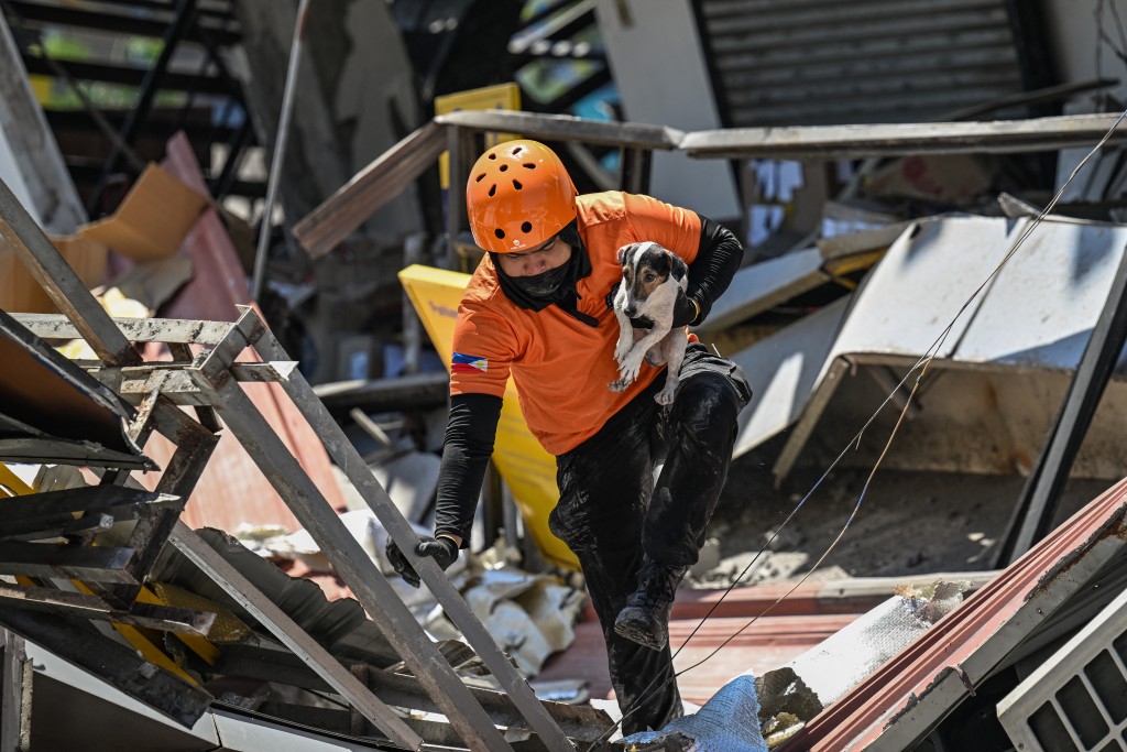 Photo by JAM STA ROSA / AFP  A responder carries a rescue dog while conducting search and rescue operations in a collapsed building after a 7.8 magnitude earthquake in General Santos City on June 9, 2026.