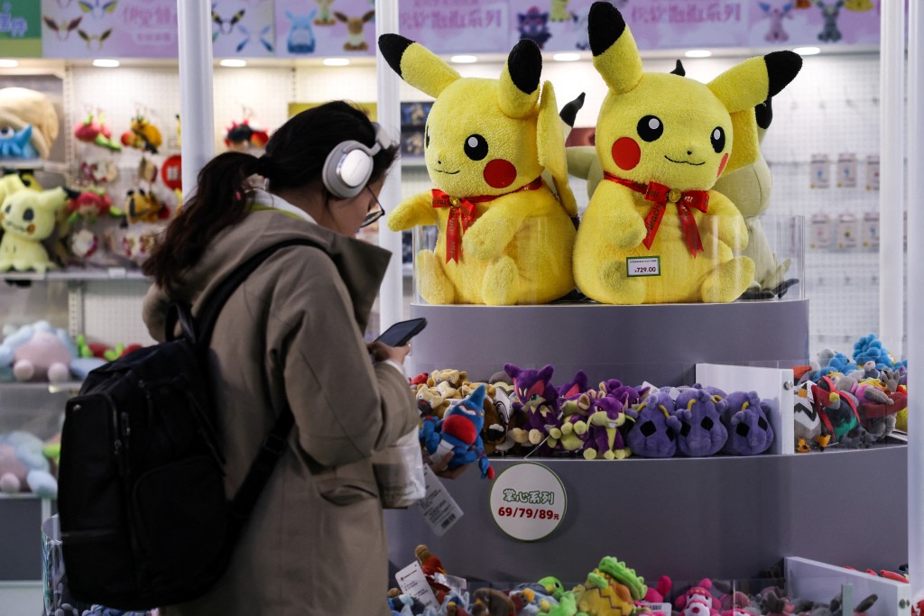 A customer looks at her phone next to stuffed toys displayed for sale, at a pop-up store of Japanese animated series "Pokemon", in a shopping mall in Beijing, China, November 18, 2025. REUTERS