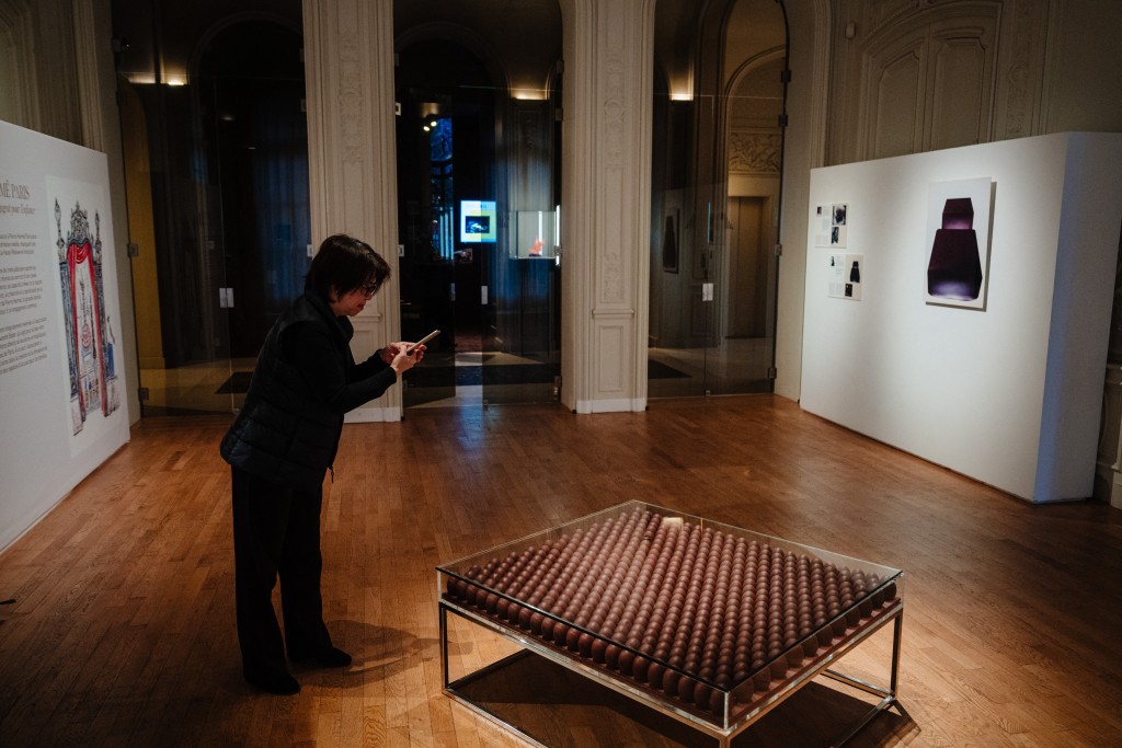 A person takes a picture of a chocolate pastry made by France's pastry chef Pierre Herme displayed on November 28, 2025 in Paris three days ahead of an auction of 25 grands chefs pastries for the benefit of the BAB Charity association, which works for the well-being and development of children with leukaemia who are hospitalised at the Armand Trousseau Hospital in Paris. (Photo by Dimitar DILKOFF / AFP)