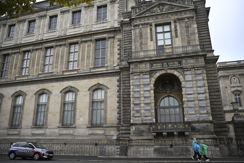 A police car is parked as people walk under the window from where entered the thieves who stole eight priceless royal pieces of jewellery from the Louvre Museum the day before, in Paris on October 20, 2025. (AFP)
