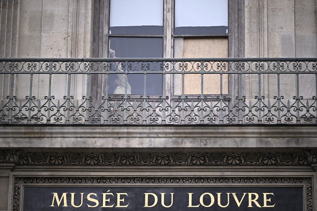 A person stands behind the window from where entered the thieves who stole eight priceless royal pieces of jewellery from the Louvre Museum the day before, in Paris on October 20, 2025. (AFP)