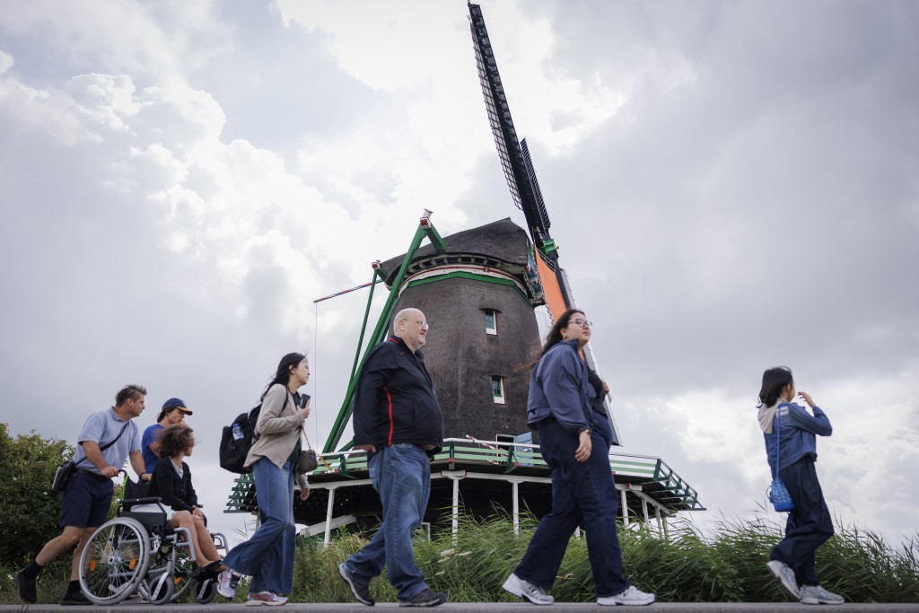 Tourists walk in front of a windmill in Zaanse Schans, on July 31, 2025. Featuring historic windmills and gabled wooden houses nestling by a meandering river, the picture perfect and TikTok famous area of Zaanse Schans is a must-see for any visitor to the Netherlands. But the village of centuries-old buildings near Amsterdam has become "a national symbol of overtourism", according to local authorities, who now want to charge a hotly contested entrance fee. (Photo by Simon Wohlfahrt / AFP)