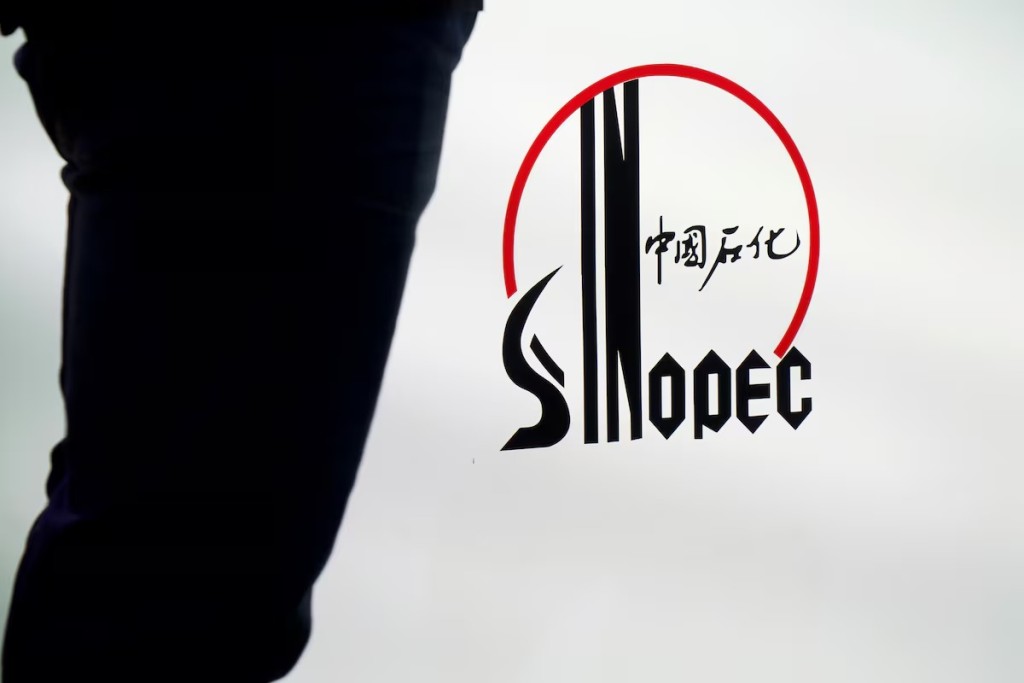 A man stands next to a logo of Sinopec, or China Petroleum and Chemical Corporation, at an expo on rubber technology in Shanghai, China September 19, 2018. Picture taken September 19, 2018. REUTERS