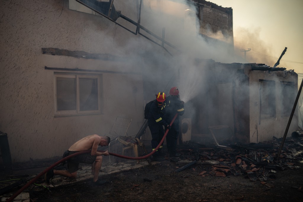 Local residents and firefighters try to extinguish the fire of a burning house during a wildfire in Kryoneri, near Athens on July 26, 2025. (AFP)