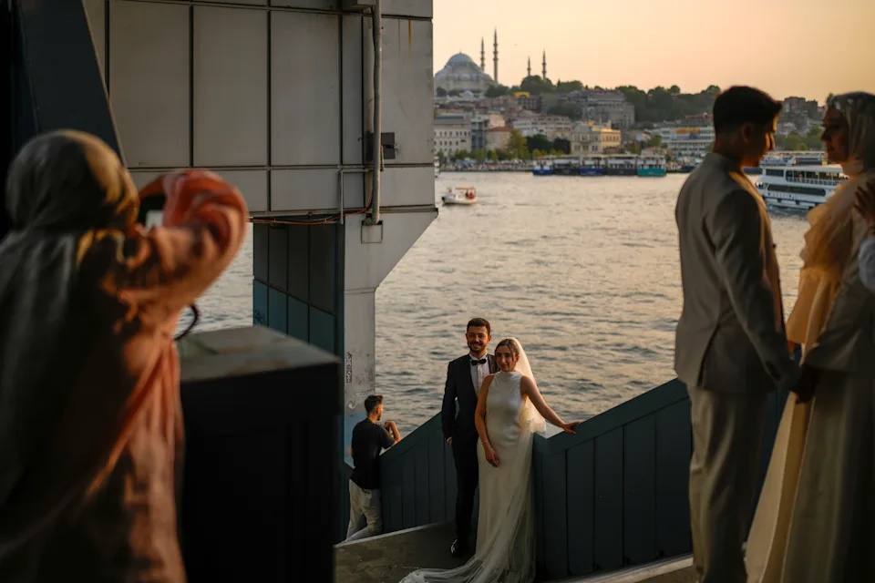 Couples wearing their wedding outfits pose during a photo session at Galata bridge, in Istanbul, Turkey, Monday, July 28, 2025. (AP Photo/Emrah Gurel)