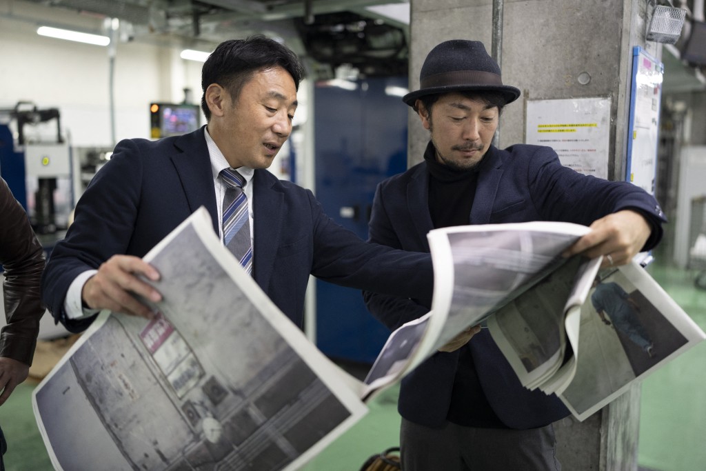 Photo by YUICHI YAMAZAKI / AFP  This picture taken on March 19, 2026 shows photographer Kazuma Obara (R) and a staff member inspecting the printing quality of his work titled “The Newspaper” at the Kyoto Shimbun factory in Kumiyama, Kyoto prefecture.