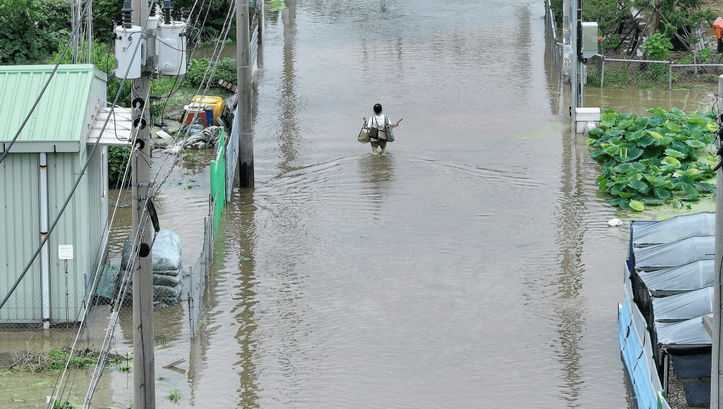 A woman carrying belongings makes her way through a flooded street due to heavy rain in Daegu, South Korea, July 10, 2024. Yonhap via REUTERS