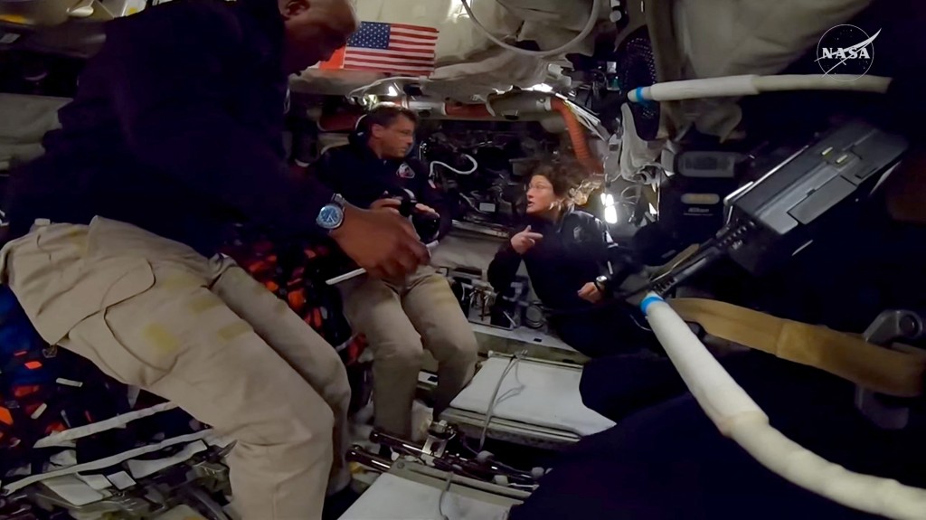 Photo by NASA / NASA / AFP  This screengrab from a NASA live broadcast video footage shows NASA astronaut and Artemis II Commander Reid Wiseman (C), NASA astronaut and Artemis II Mission Specialist Christina Koch (R) and NASA astronaut and Artemis II pilot Victor Glover working inside the Orion spacecraft as they pass the halfway point between Earth and the Moon on the way to their planned lunar flyby in the Orion spacecraft, on April 3, 2026.