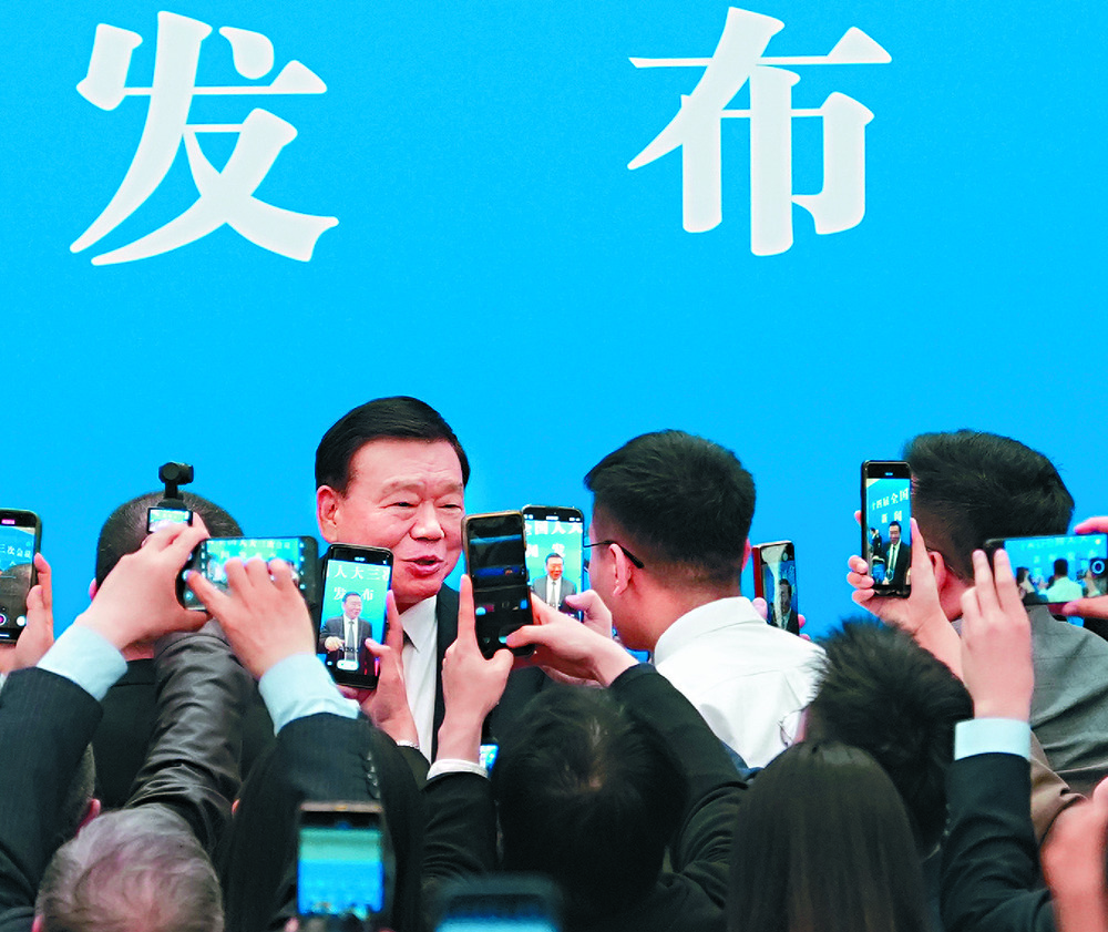 Lou Qinjian answers questions from the media as Wang Huning, inset, delivers his report. XINHUA