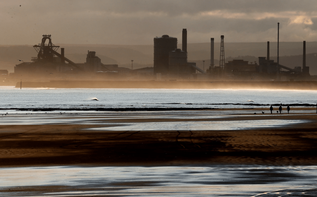 FILE - People walk their dogs on the beach, with the backdrop of the Redcar steel plant in the background, in Hartlepool, England, Nov. 12, 2019. (AP Photo/Frank Augstein, File)