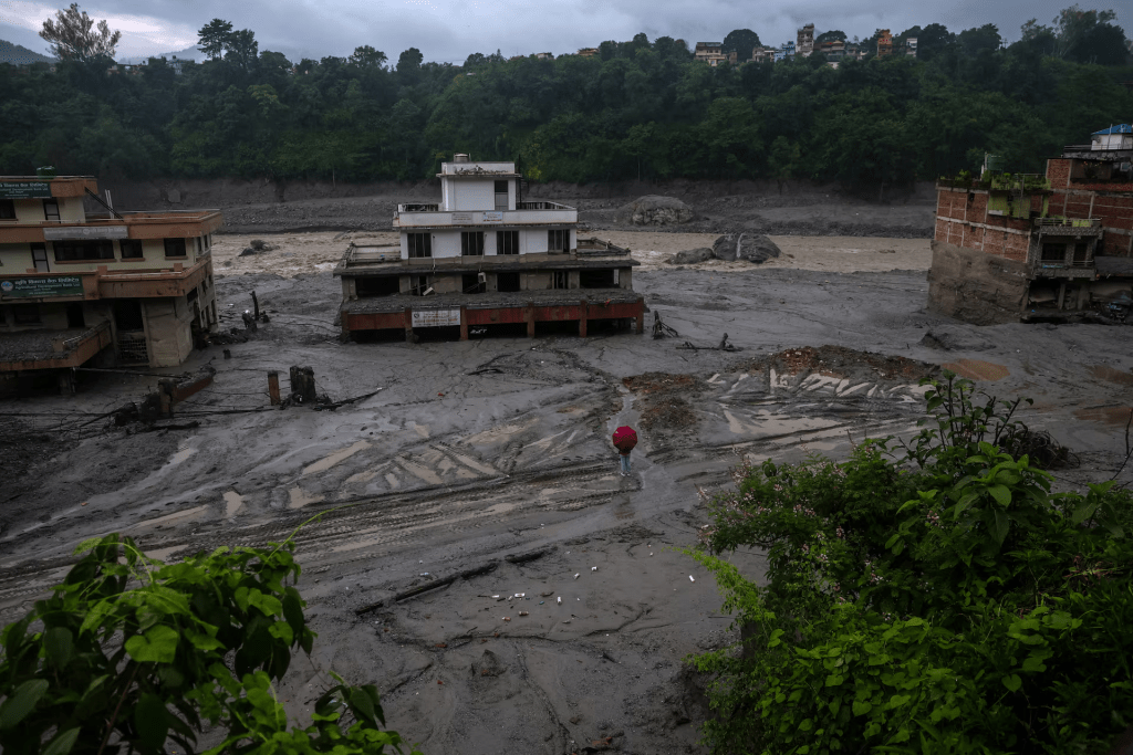 A person holds an umbrella as he stands in front of damaged buildings after flash floods and a mudslide, in Trishuli, Nuwakot district, Nepal, August 29, 2026. REUTERS/Athit Perawongmetha