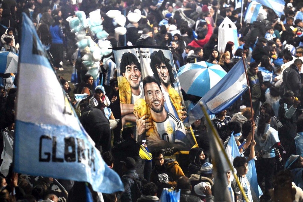 Fans hold a banner depicting Argentine football legends Diego Maradona, Mario Kempes and Lionel Messi holding FIFA World Cup trophies as supporters gather near the Argentine Football Association (AFA) training camp in Ezeiza, Buenos Aires Province, on July 20, 2026, while awaiting the arrival of Argentina's national football team from the United States following its defeat in the 2026 FIFA World Cup final. (Photo by Luis ROBAYO / AFP)