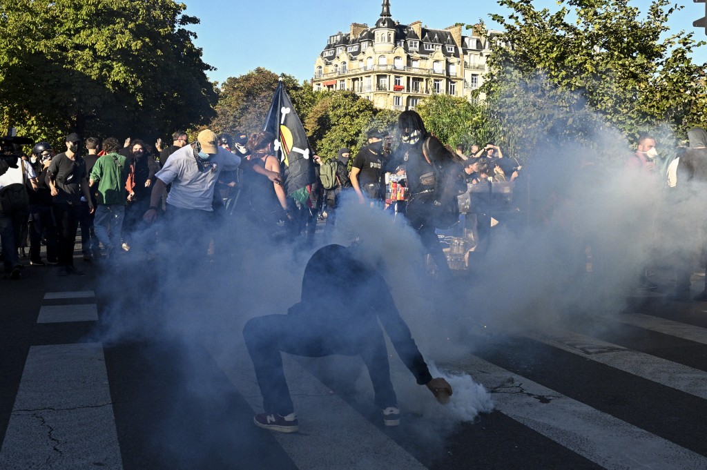 A protestor takes a tear gas canister fired by French police in Paris, on September 18, 2025, during a day of nationwide strikes and protests called by unions over France's national budget. (Photo by JULIEN DE ROSA / AFP)