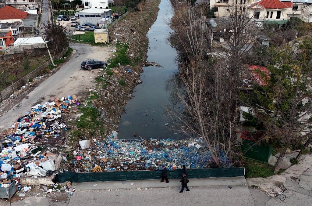 Photo by ADNAN BECI / AFP  Local residents walk on a bridge, above plastic trash-filled floodwaters following heavy rains, in Durres, on January 13, 2026.