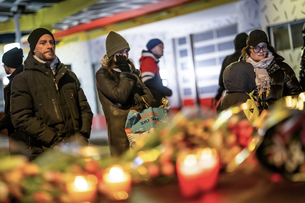 Mourners gather in front of flowers and candles laid near the site where a fire ripped through a crowded bar during New Year's Eve celebrations in the Alpine ski resort town of Crans-Montana on January 1, 2026. (AFP)