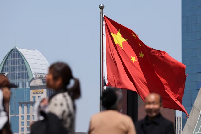 A Chinese national flag flies as people walk on a pedestrian bridge at the Lujiazui financial district in Shanghai, China April 15, 2025. REUTERS/Go Nakamura 