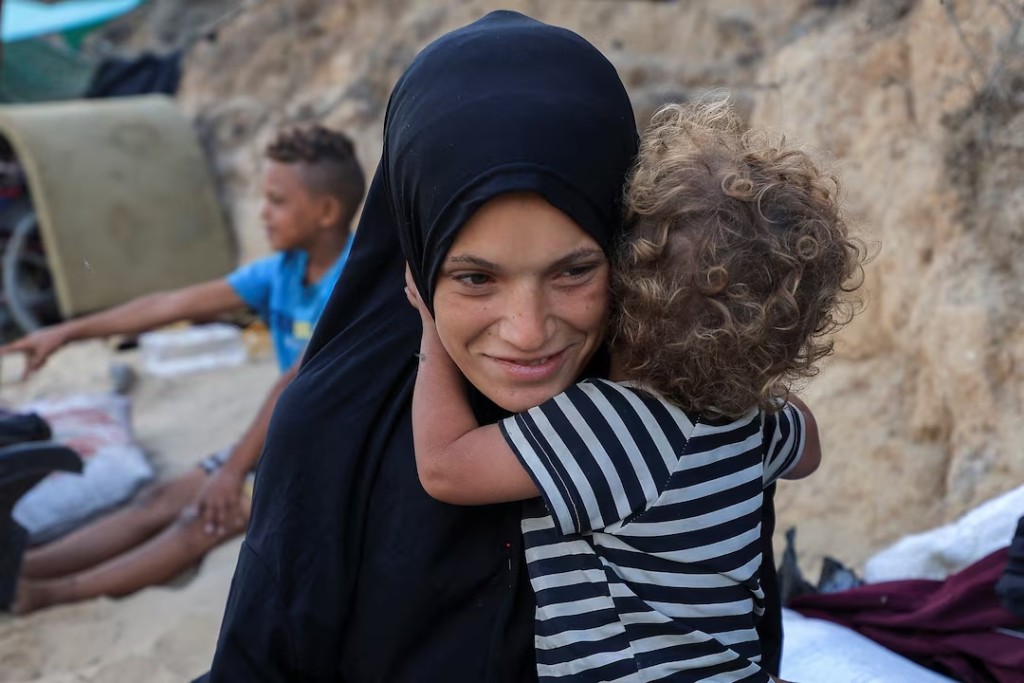 Palestinian woman Nancy Abu Matroud, who fled Gaza City recently due to an Israeli military operation and went into labor while moving south then gave birth prematurely to twins who later died, plays with her daughter Etra, a cancer patient, as they shelter by a roadside, in the central Gaza Strip September 26, 2025. REUTERS/Dawoud Abu Alkas