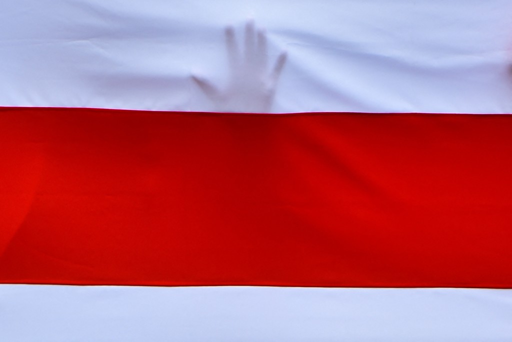 (FILES) A hand of a protester touches a historical white-red-white flag of Belarus during a march of workers of the Belarusian Automobile Plant (BelAZ) in support of victims of security forces arbitrary and striking workers across the country in the town of Zhodino on August 26, 2020. (Photo by Sergei GAPON / AFP)