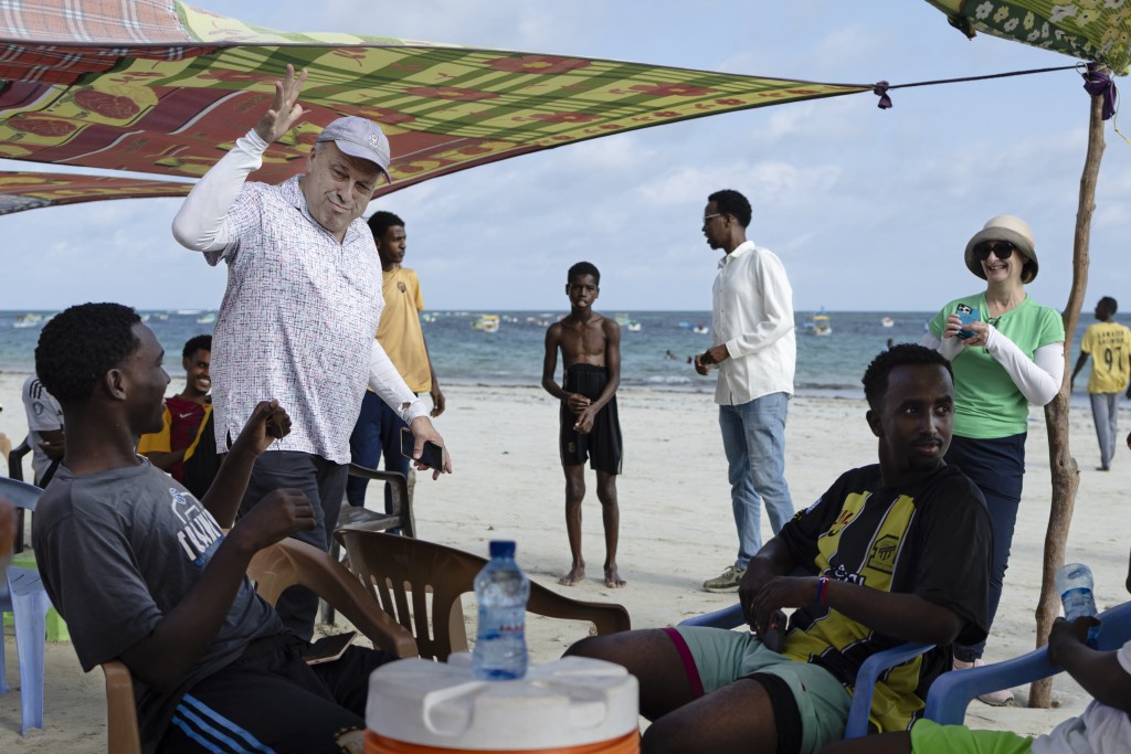 Photo by TONY KARUMBA / AFP US tourists Richard (2nd L) and Sheryl (2nd R) interact with local youth on their walk on Lido beach during a guided tour of tourist attractions in Mogadishu on November 10, 2025.