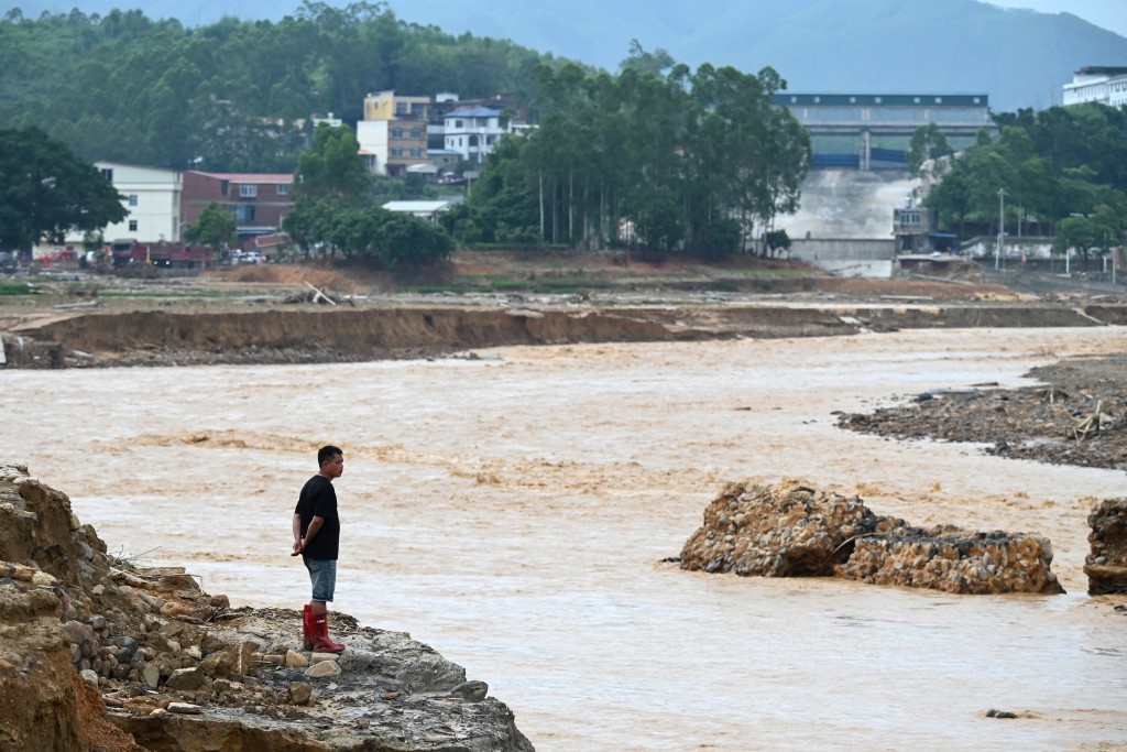 Photo by GREG BAKER / AFP  A man looks at water flowing from the collapsed Liulan reservoir in Liulan village in Hengzhou city, China’s southwest Guangxi region, on July 8, 2026.