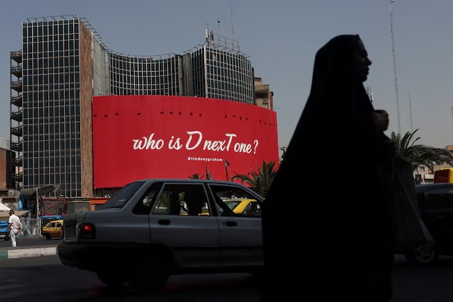 A woman walks near a billboard with a slogan referring to U.S. President Donald Trump and a hashtag referring to late U.S. Senator Lindsay Graham, in Tehran, Iran, July 27, 2026. Majid Asgaripour/WANA (West Asia News Agency) via REUTERS