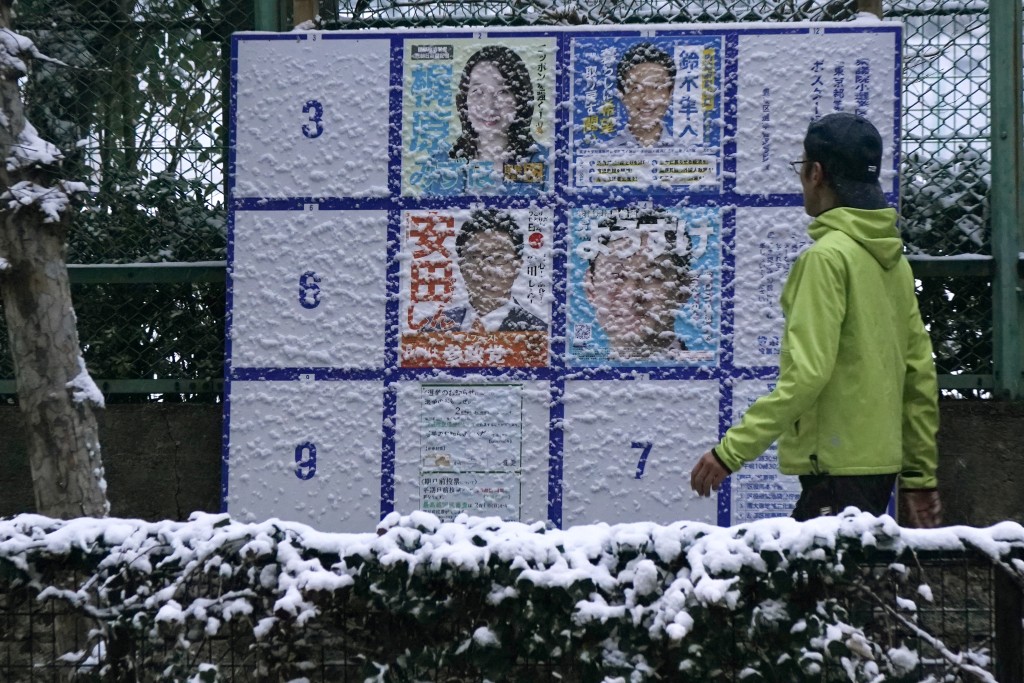 A man walks past a board displaying posters of candidates for the Lower House election, which is being held February 8, along the street amidst the falling snow in Tokyo, on February 8, 2026. (AFP)