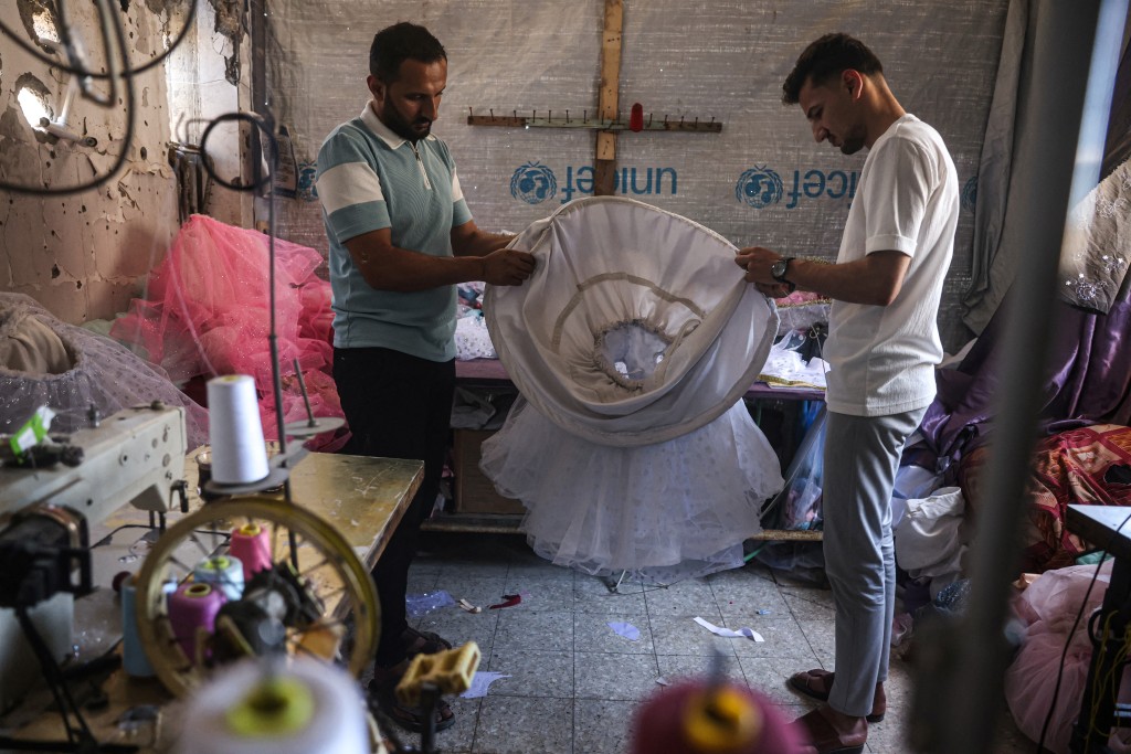 Photo by BASHAR TALEB / AFP Palestinian dressmakers add skirt hoops to a child's gown, at a workshop where dresses are created including evening and wedding gowns despite limited resources and old dresses are recycled, in the city of Khan Yunis in the southern Gaza Strip on June 13, 2026.