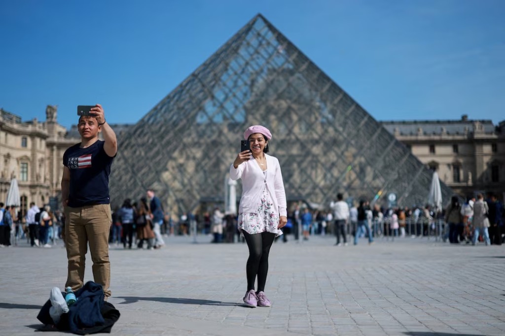 Tourists take selfies in front of the glass Pyramid of the Louvre museum on a sunny spring day in Paris, France, April 22, 2026. REUTERS/Stephanie Lecocq/File Photo